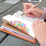 
A girl writing on midori style traveler's notebook with boho feathers design on a wooden table