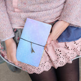 
a young girl showing midori style traveler's notebook with ombre pastel galaxy design above her leg